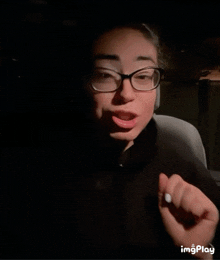a woman wearing glasses is making a funny face in a dark room with the words imgplay below her