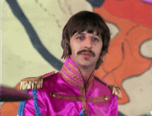 a man with a mustache wears a pink jacket with gold trim
