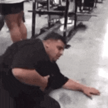 a man is kneeling on the floor in a gym while a woman stands behind him .
