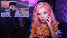 a woman with pink hair is sitting in front of a screen with a cartoon of a man with a beard on it