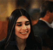 a woman is smiling and looking at the camera while a man stands in the background .