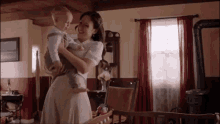 a woman is holding a baby in her arms and smiling in a room .