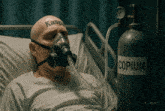 a man wearing a gas mask is laying in a hospital bed next to a bottle of copium