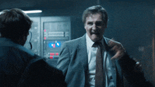 a man in a suit and tie talks to another man in a dark room