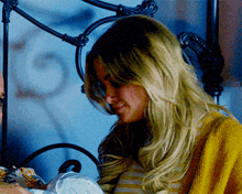 a woman in a yellow sweater is holding a baby in front of a bed