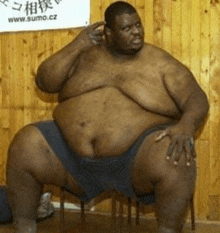a sumo wrestler is sitting on a chair in front of a wooden wall and talking on a cell phone .