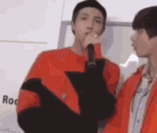 a man in a red shirt is holding a microphone and talking to another man in an orange jacket .