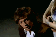 a man in a brown jacket and white shirt is being held by a woman