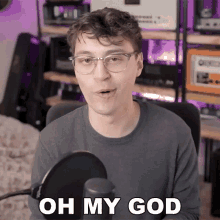 a man with glasses is talking into a microphone with the words oh my god above him