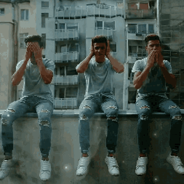 three men are sitting on a wall with their hands over their ears