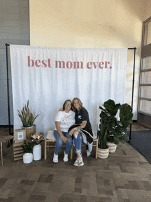 two women are posing for a picture in front of a banner that says best mom ever