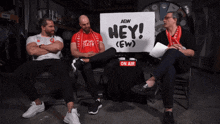 three men are sitting in front of a sign that says hey ( ew )