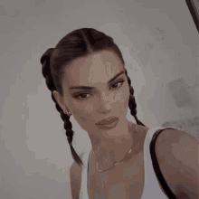 a woman with braids in her hair is wearing a white tank top and a gold necklace