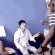 a man in a white shirt is sitting on a blue couch talking to another man