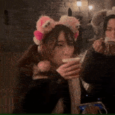 a woman wearing a headband with stuffed animals on it is drinking from a cup