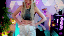 a woman wearing headphones and a crop top is standing with her hands on her hips in a room with a purple background