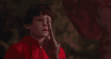 a young boy in a red jacket is looking at an alien 's hand with a red light coming out of it .
