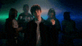 a man in a black jacket is dancing in a dark room with people behind him .