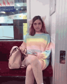 a woman wearing a rainbow colored sweater is sitting on a bench with her legs crossed