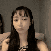 a woman with long black hair and bangs is sitting on a couch
