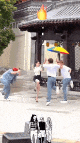a group of people are dancing in front of a building with a rainbow colored umbrella