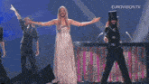 a woman in a white dress and a man in a top hat are on a stage with eurovision.tv written on the bottom right