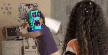 a girl with curly hair is standing in front of a computer with a pixelated image of a robot on her head