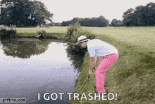 a man in pink pants is holding a golf club next to a body of water and says " i got trashed "
