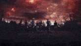 a group of people are dancing in a field with fireworks exploding in the background