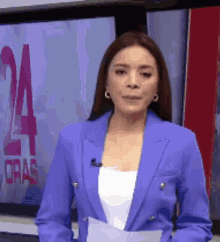 a woman in a blue jacket is standing in front of a television screen with the number 24 on it .