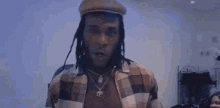 a man with dreadlocks wearing a hat and a plaid shirt is standing in a room .