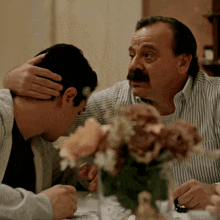 a man with a mustache talks to another man while sitting at a table