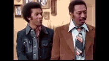 two men are standing next to each other in a living room .
