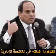 a man in a suit and tie is holding a microphone and giving a thumbs up sign