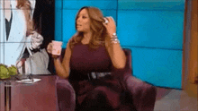 a woman in a purple dress is sitting in a chair holding a cup of coffee