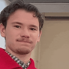 a man in a red sweater and plaid shirt is making a funny face .