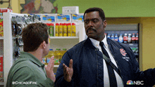 a man in a bomber jacket talks to another man in a store