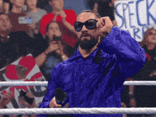 a man in a blue jacket and sunglasses stands in a wrestling ring