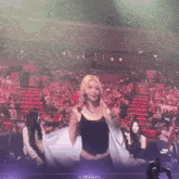 a woman in a black tank top is standing in front of a crowd in a stadium .