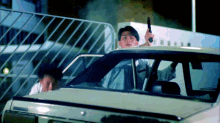 a man in a car holds a gun in front of a building