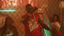 a man in a red jersey with the number 12 on it is behind a chain link fence