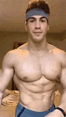 a shirtless man wearing a headband and blue shorts is flexing his muscles .