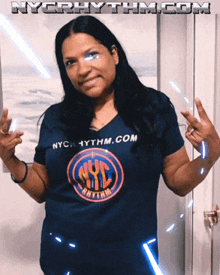 a woman wearing a nyc rhythm shirt stands in front of a wall