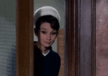 a woman is standing in a doorway wearing a white hat and a blue shirt .