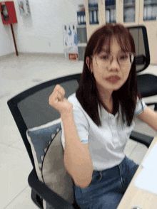 a woman wearing glasses is sitting at a desk with her fist up