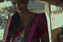 a woman wearing a saree and a red blouse is smiling and looking down