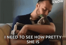 a man is sitting on a couch holding a cat and says `` i need to see how pretty she is '' .