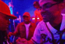 a man wearing glasses and a baseball jersey is talking to another man in a dark room .