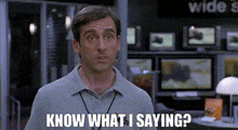 a man in a grey shirt is standing in front of a computer monitor and says `` know what i saying ? ''