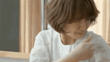 a woman in a white shirt is sitting at a table with her eyes closed and looking down .